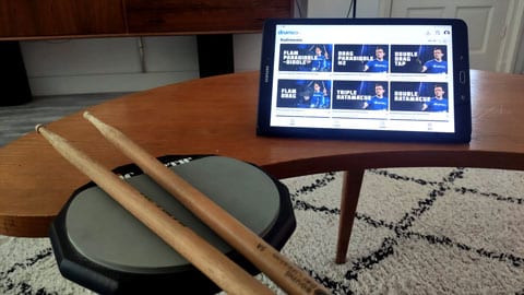 Een Drumeo setup met een tablet en een oefenpad met daarop drumstokken.