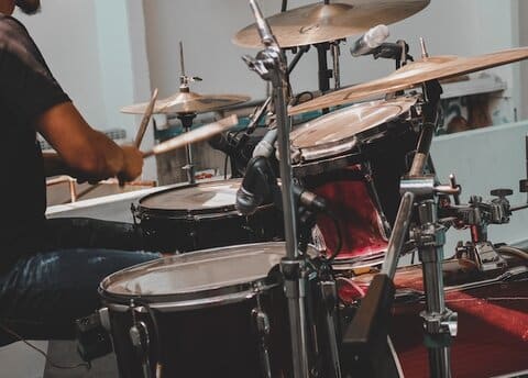 Een drummer die online drumles volgt achter een rood drumstel.